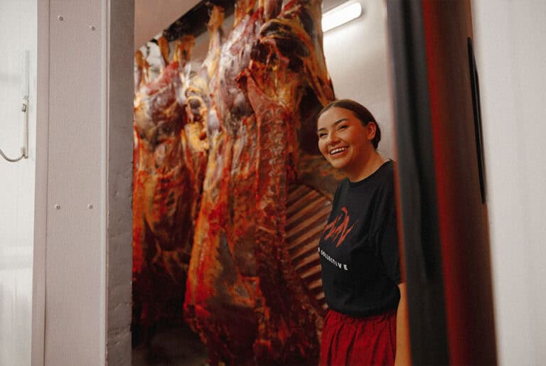 Smiling Indigenous Female standing next to a hanging buffalo carcuss